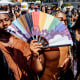People dance and someone holds a rainbow hand fan outside during an event